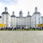 Eine große Gruppe von Menschen, bestehend aus Köchinnen, Köchen und Veranstaltungsbeteiligten, steht vor der beeindruckenden Fassade des Althoff Grandhotel Schloss Bensberg. Die Teilnehmer sind in einer langen Reihe auf dem Kopfsteinpflaster vor dem Schloss positioniert.