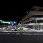 Eine nächtliche Szene der Las Vegas F1 Grand-Prix-Strecke mit mehreren Bugatti-Fahrzeugen, die an der Boxengasse vorbeifahren, beleuchtet von Heineken- und Rolex-Werbung.