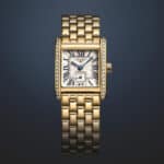 Das Foto zeigt eine goldene Longines Mini DolceVita Uhr mit Diamantbesatz auf dunklem Hintergrund