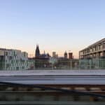 Blick über eine Bahnstrecke auf die Kölner Skyline mit dem Kölner Dom, Stadttor und modernen Gebäuden bei Sonnenuntergang.